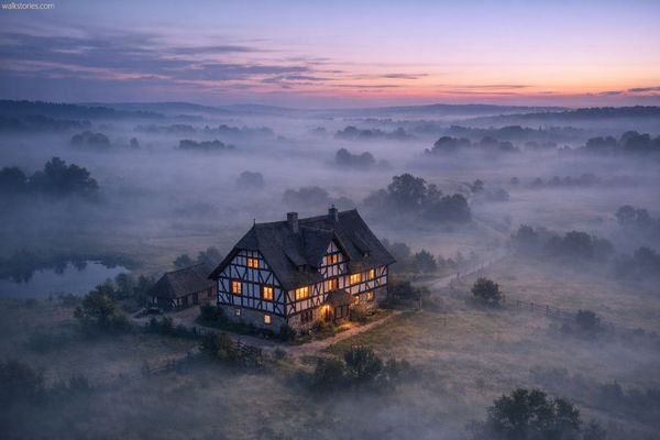 Maison à colombages isolée dans la campagne normande plongée dans la brume au crépuscule